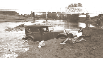 William Sibley examining a tourist’s car stuck in the river. The driver was trying to cross the Yass River after the bridge approach was washed away in 1925. The damaged bridge is shown in the background